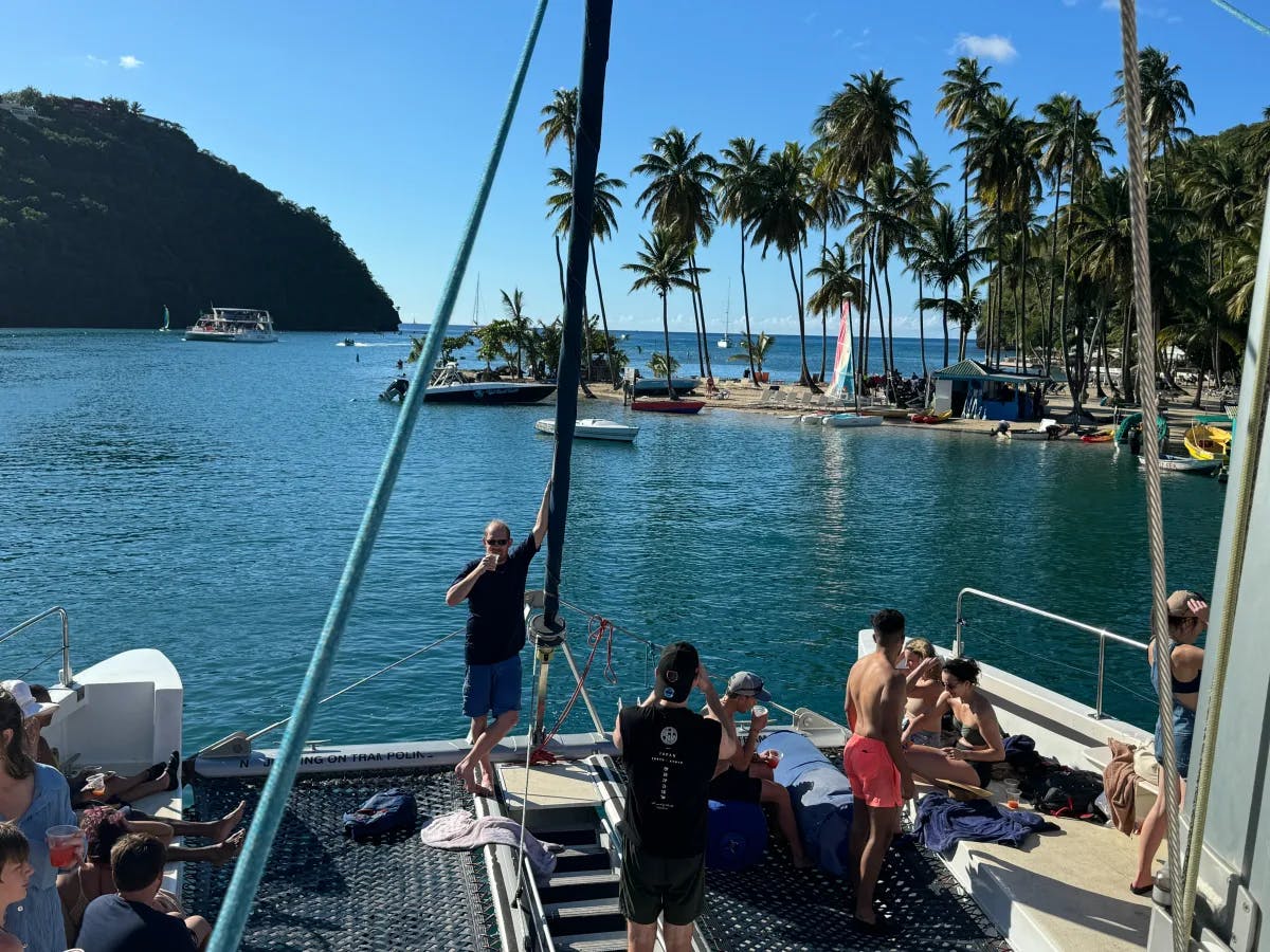 A group of people enjoys a sunny day on a boat with a view of the sea, other boats and a green hill in the background.