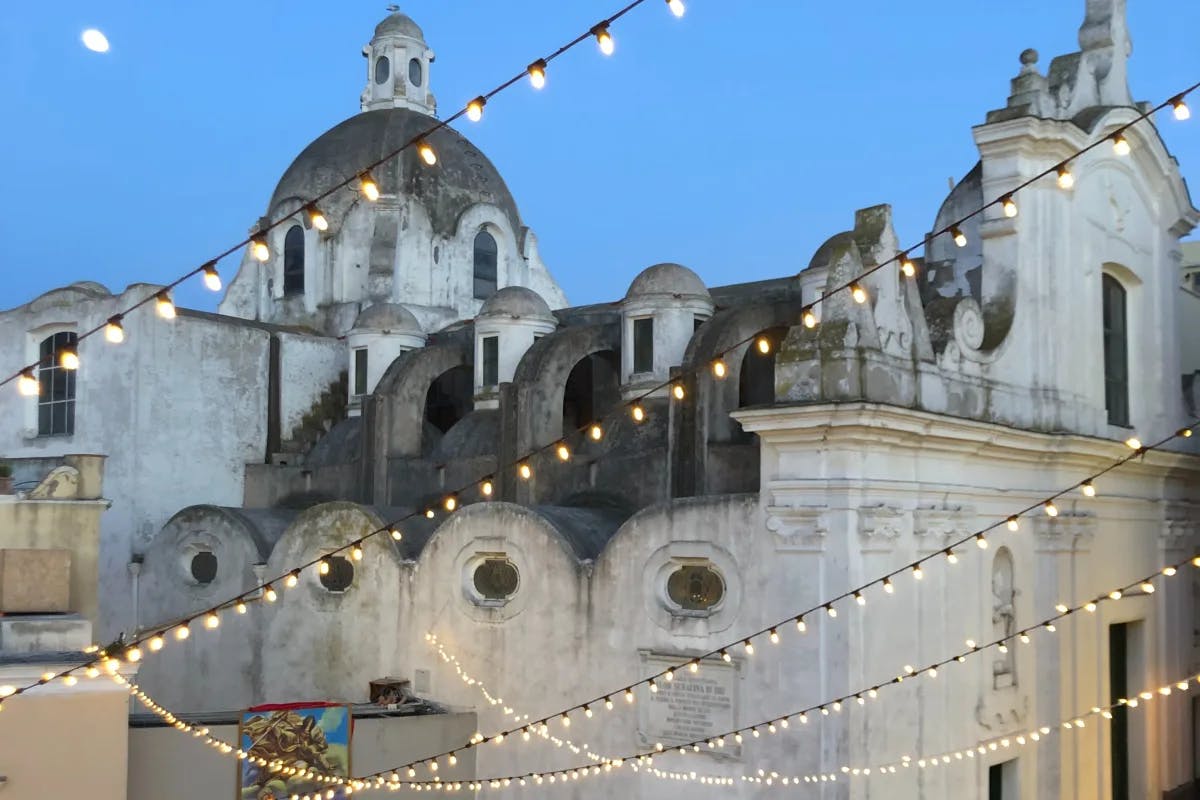 View from Ristorante Pulalli – string lights with a large stone building with multiple domes in the background