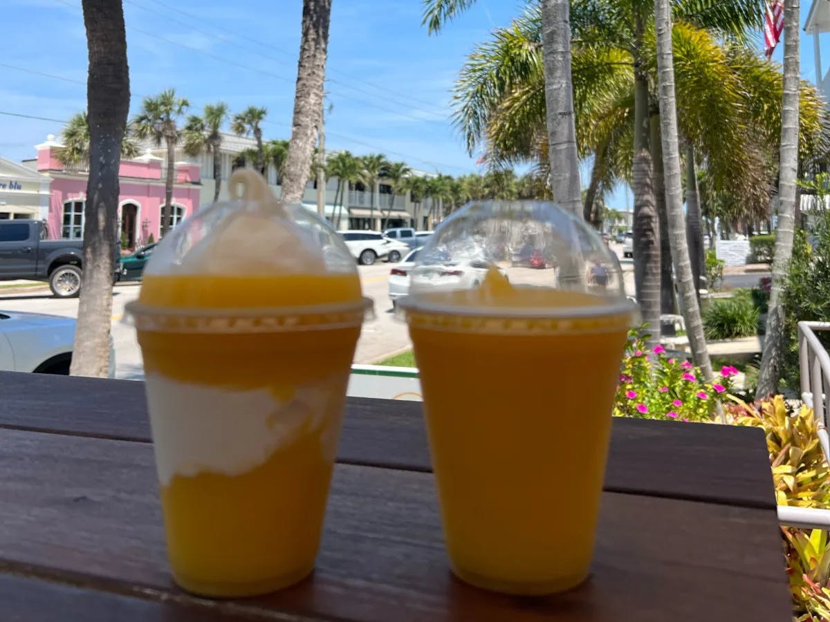 Orange colored drink in two disposable glasses.