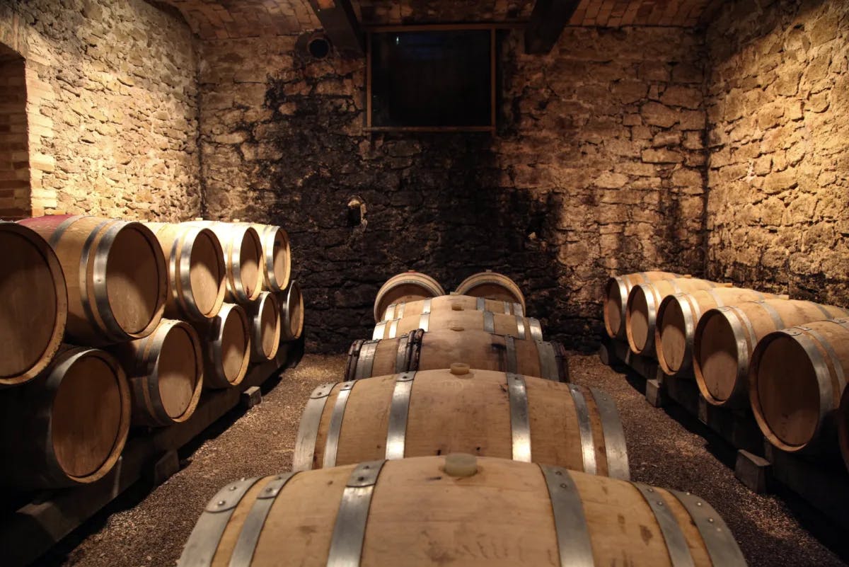 A wine cellar full of wooden barrels stacked together against a stone wall. 