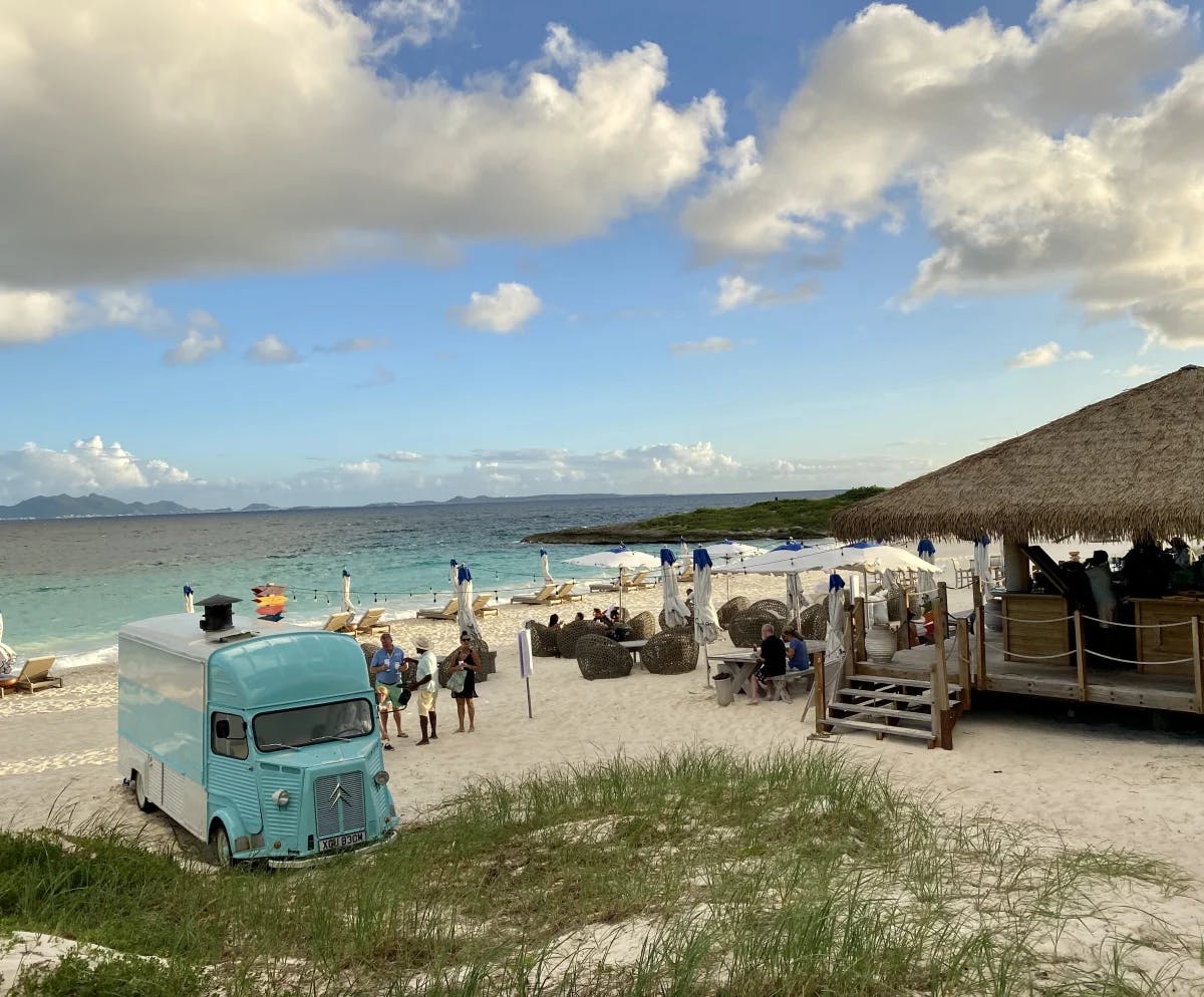 An outdoor covered restaurant on the beach with a turquoise food truck