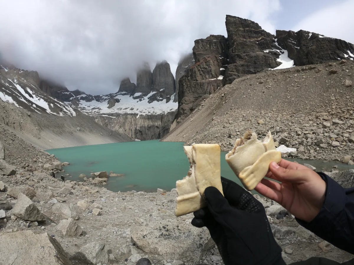 Sharing  empanadas in front of a green lake among snow covered mountain peaks. 