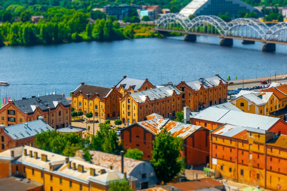 A stunning aerial view of Riga, complete with a bridge, warm-toned buildings and a large canal in the background surrounded by trees and a town.