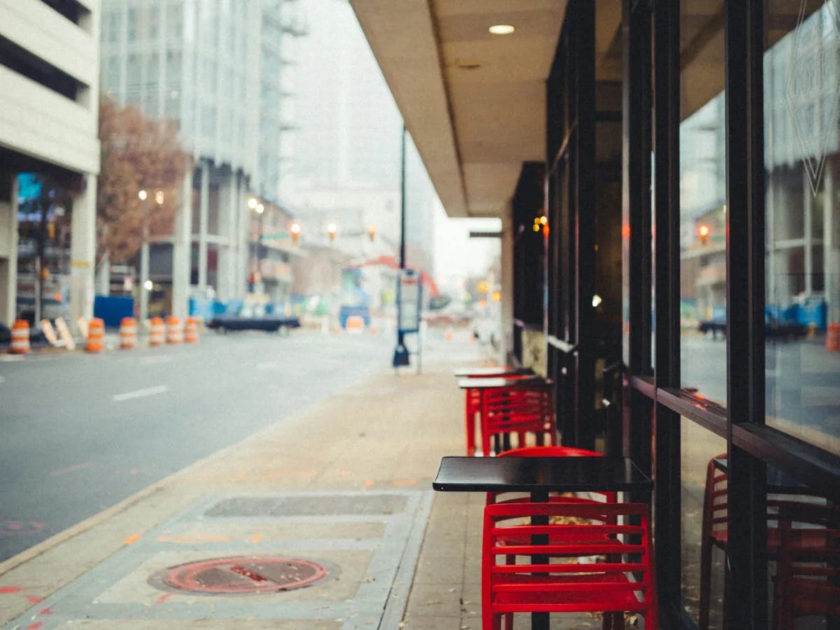 Red chairs and tables outside of a café near a sidewalk downtown.