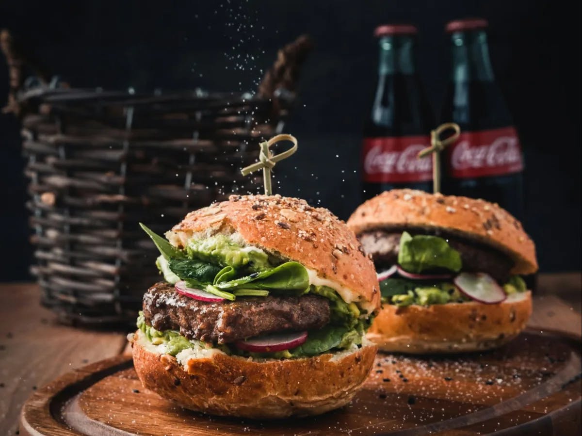 Two burgers with meat patties and two coca cola glass bottles. 