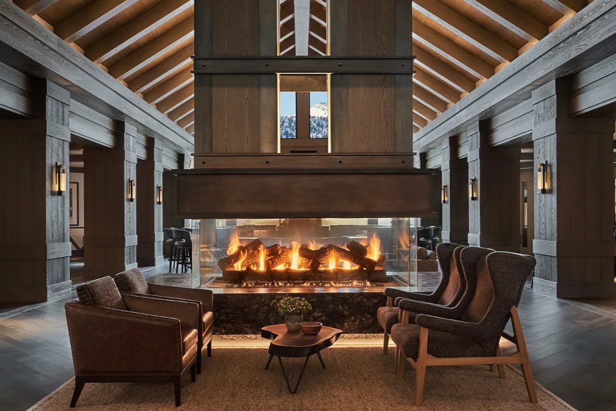 a fancy hotel lobby with a central fire place amid wooden floors and towering beamed ceilings