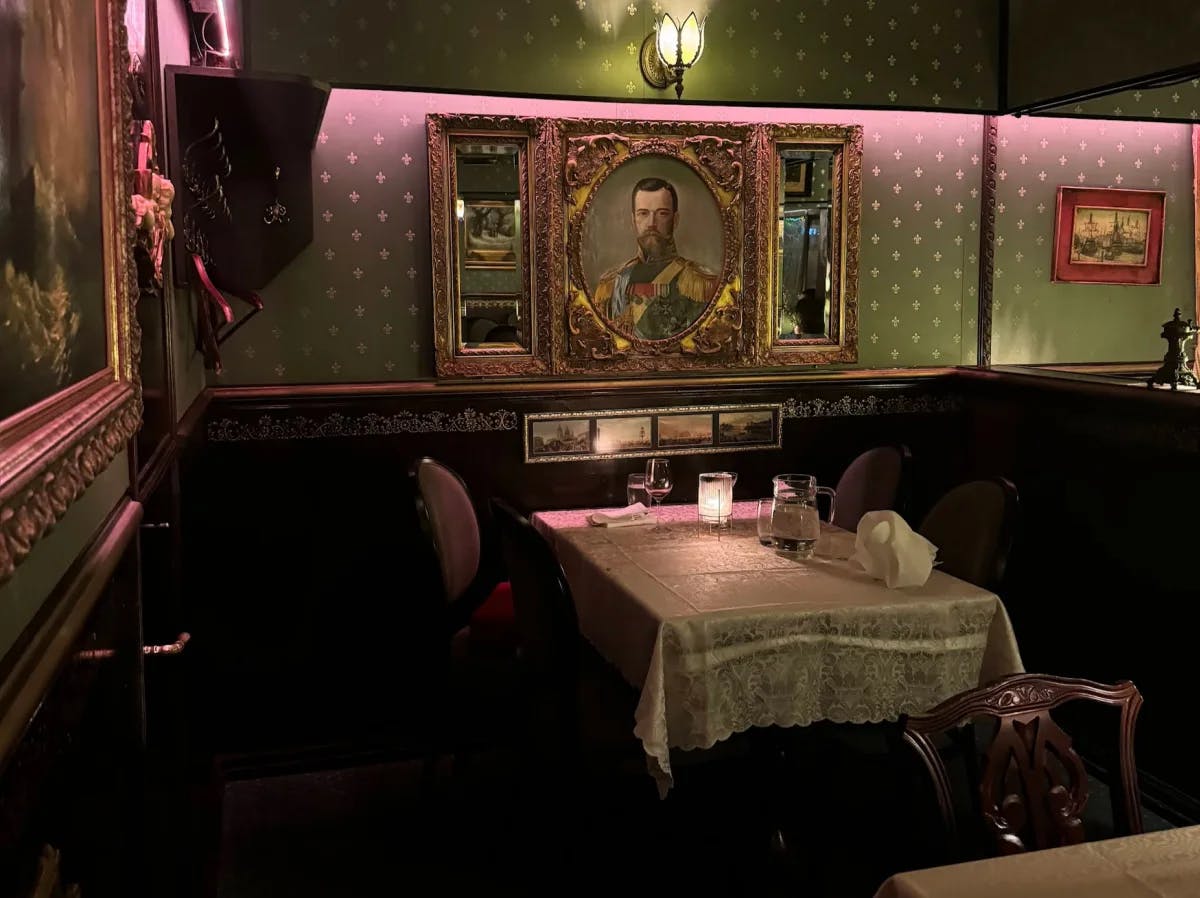 A candlelit restaurant interior with a table set with a lace tablecloth, green wallpaper and a portrait of a military general on the wall.