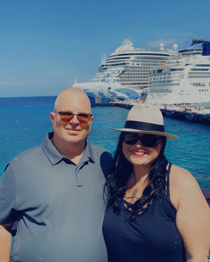 Advisor and wife posing in the sun with a cruise ship in the background