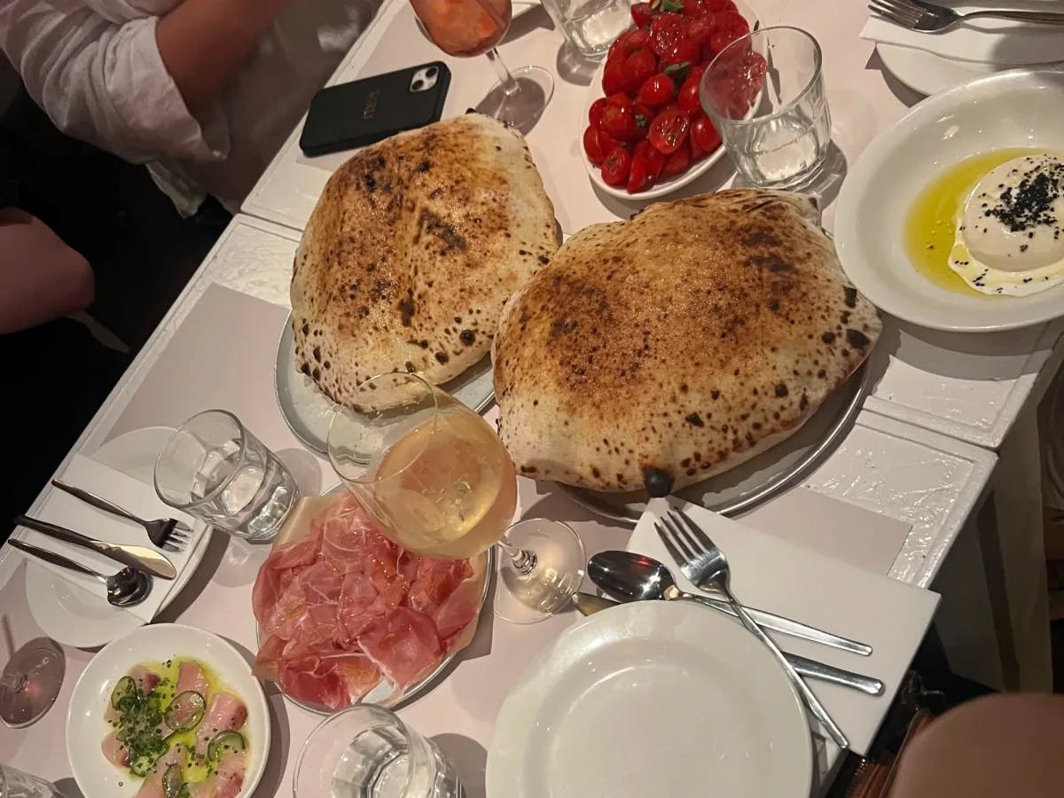 A table with large loaves of bread, a bowl of tomatoes, a plate of cured meat and wine glasses.