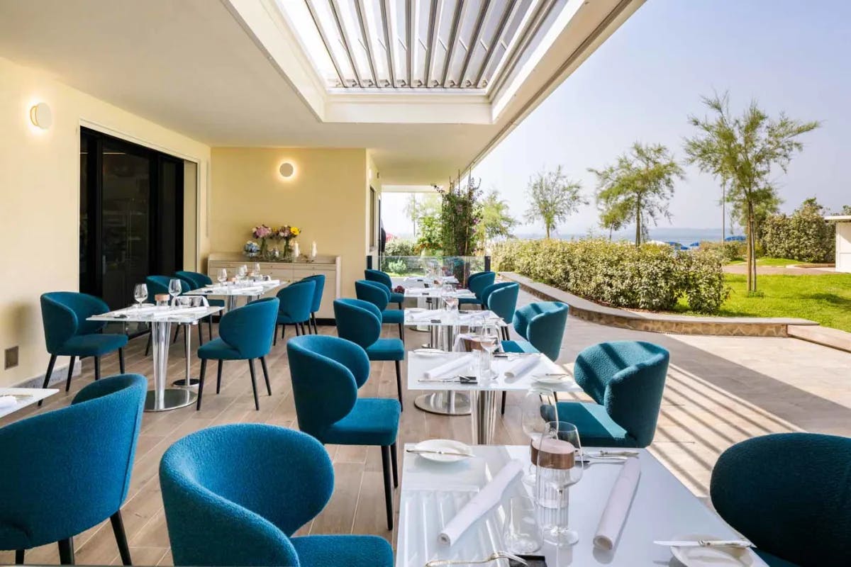 an outdoor restaurant with blue chairs and white tables overlooking the sea