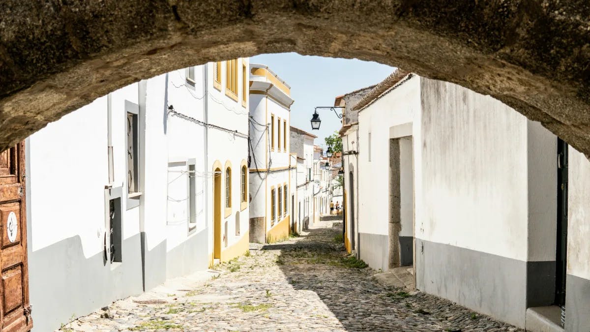 Street of an old town surrounded by buildings, a brick road and a stone archway. 