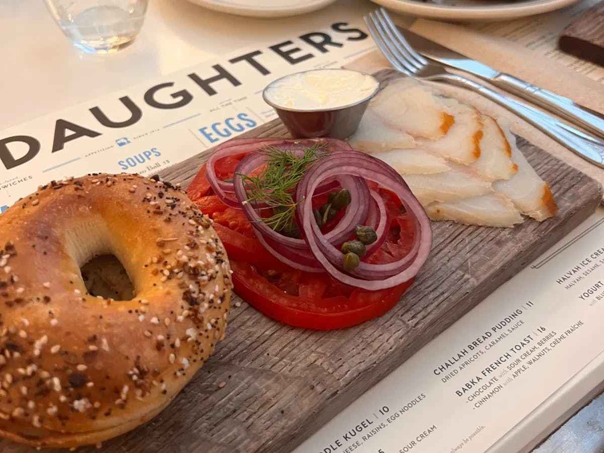 A platter with bagel, fish, tomatoes and sauce.