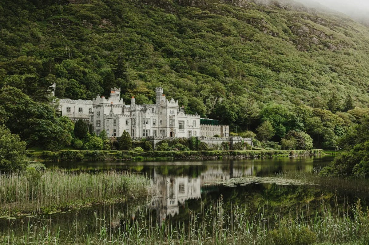 Kylemore Abbey, a large white castle on a lake with green hills surrounding it.