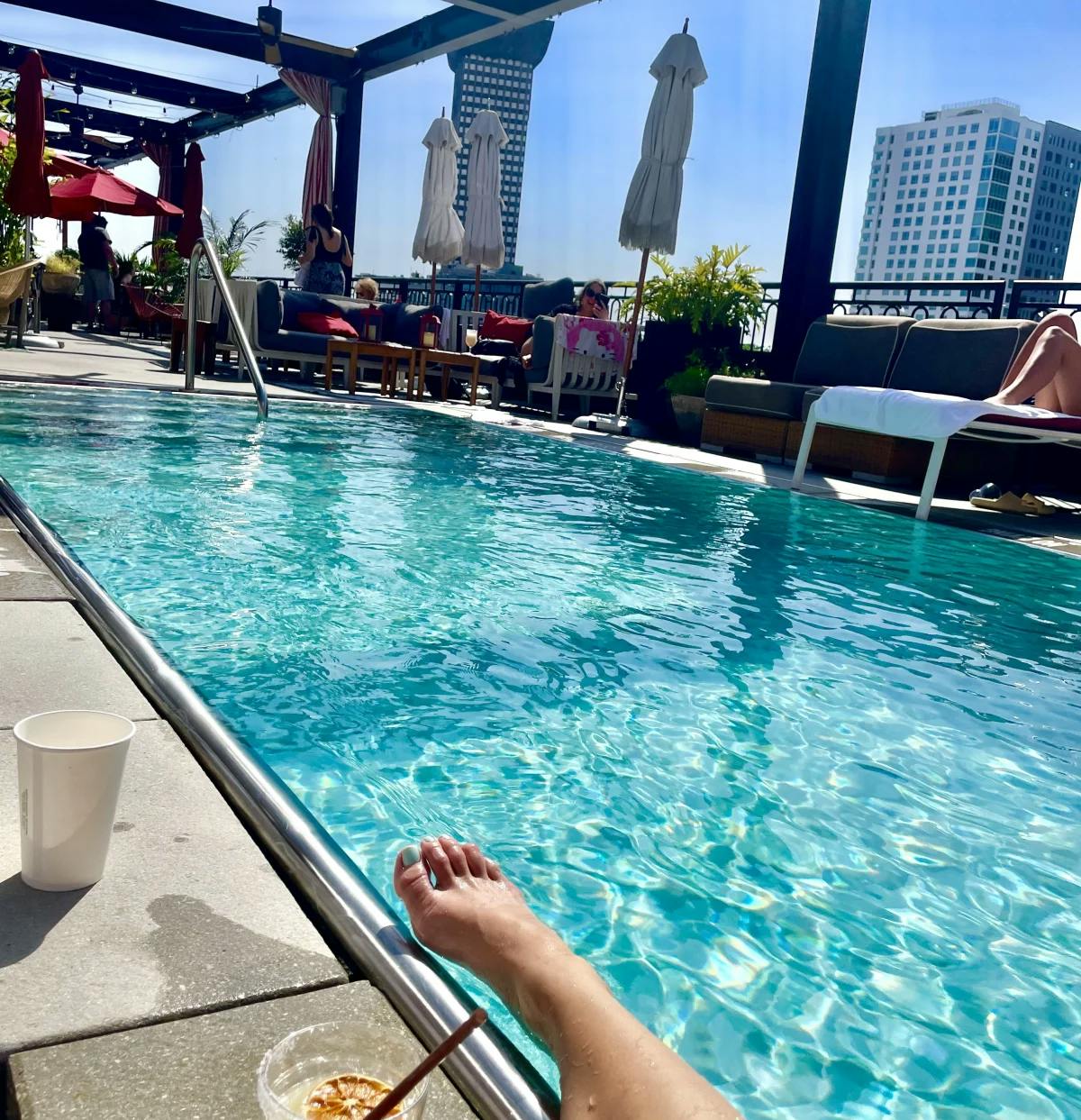 A pool on the roof with a cocktail in the foreground and buildings in the background.