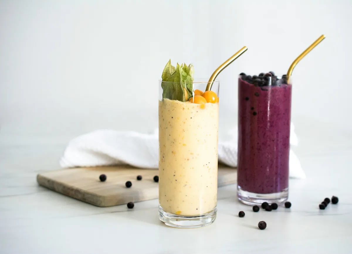 Two glasses of smoothies, one yellow and one berry-colored, with a small wooden board and napkin.