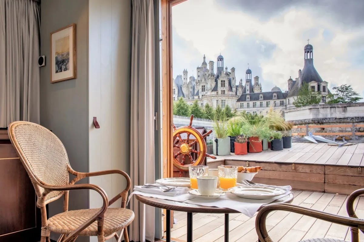 breakfast table with two chairs looking onto a terrace with a castle in the background