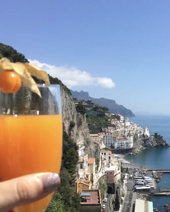 An orange cocktail held up in front of a coastline