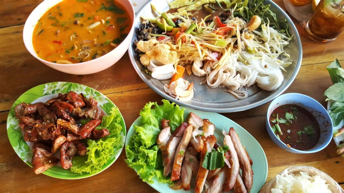 A picture of multiple plates of Thai food dishes on top of a wooden table. 