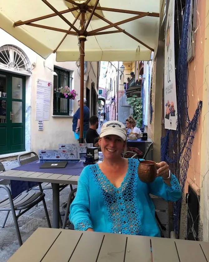 Travel advisor Shannon in a blue shirt and hat sitting at an outdoor cafe in a narrow street