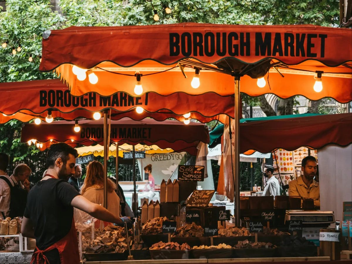 A vibrant Borough Market scene with vendors, red tents, and a variety of goods, creating a lively and inviting atmosphere.