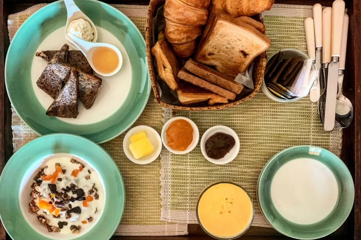 A breakfast spread with bread, jam, butter, pastries and cereals set out on a table. 