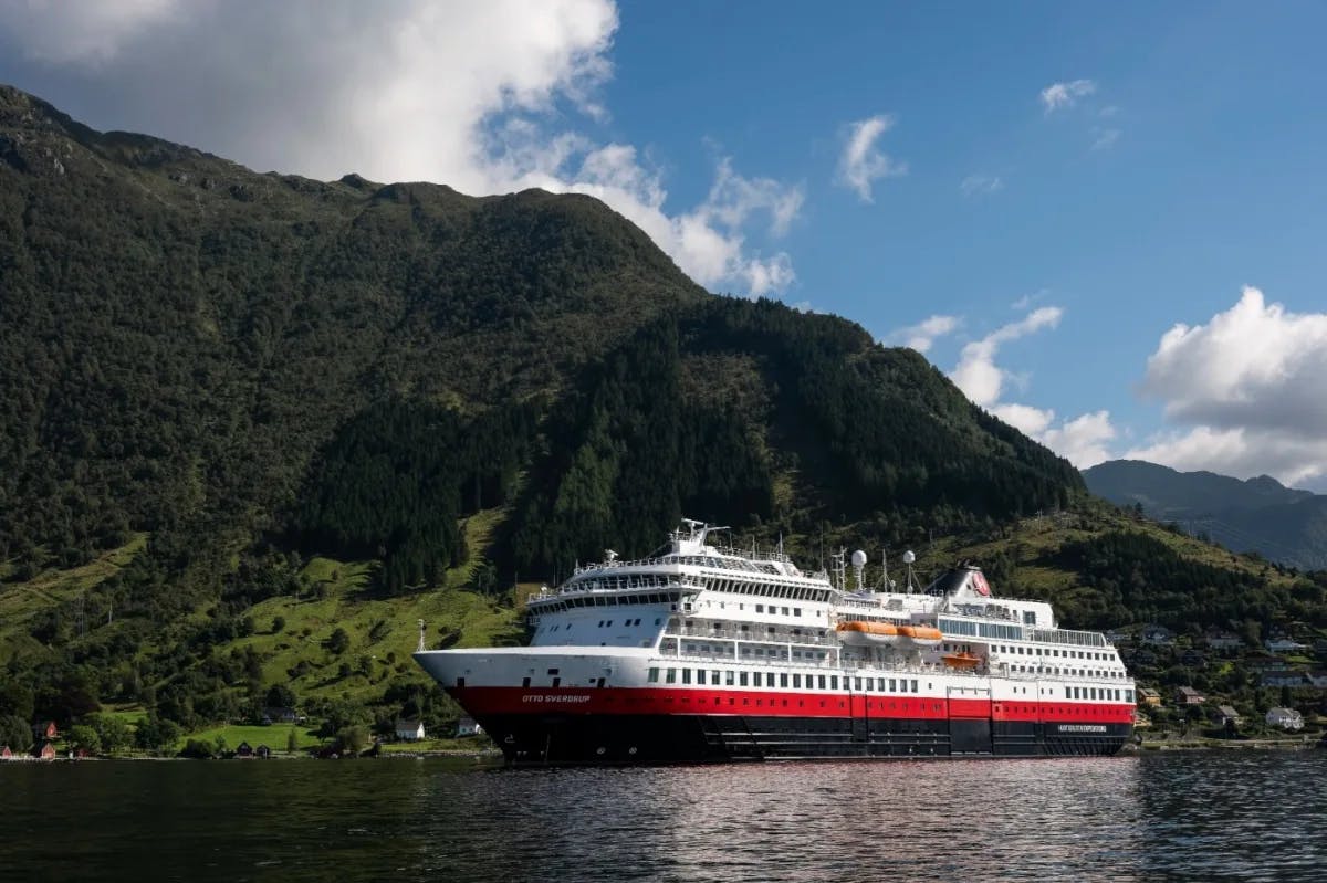 red, white and blue ship with a green mountain and blue sky behind it