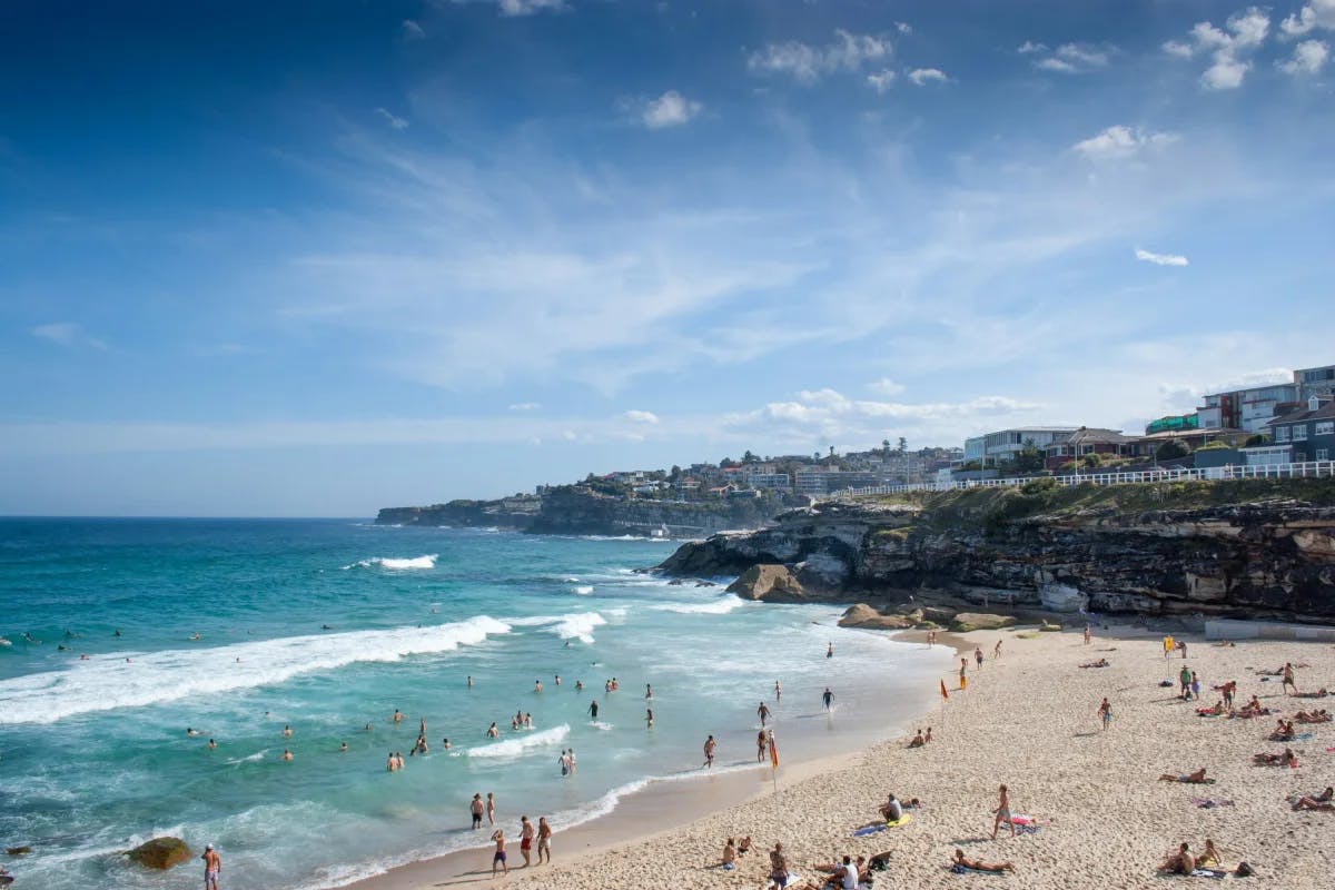 A vibrant beach scene with people relishing the sun and sea against rocky cliffs and coastal buildings.