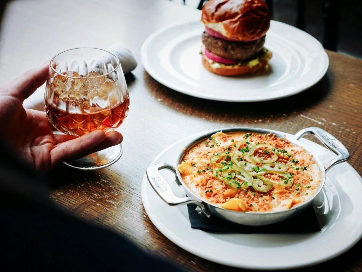 A wooden table with a burger, dish of macaroni and cheese and a cocktail.