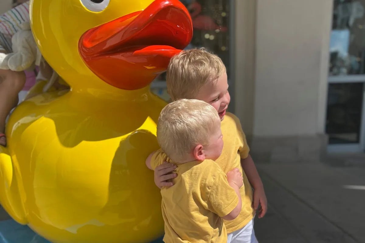 Two children posing with a large duck mascot