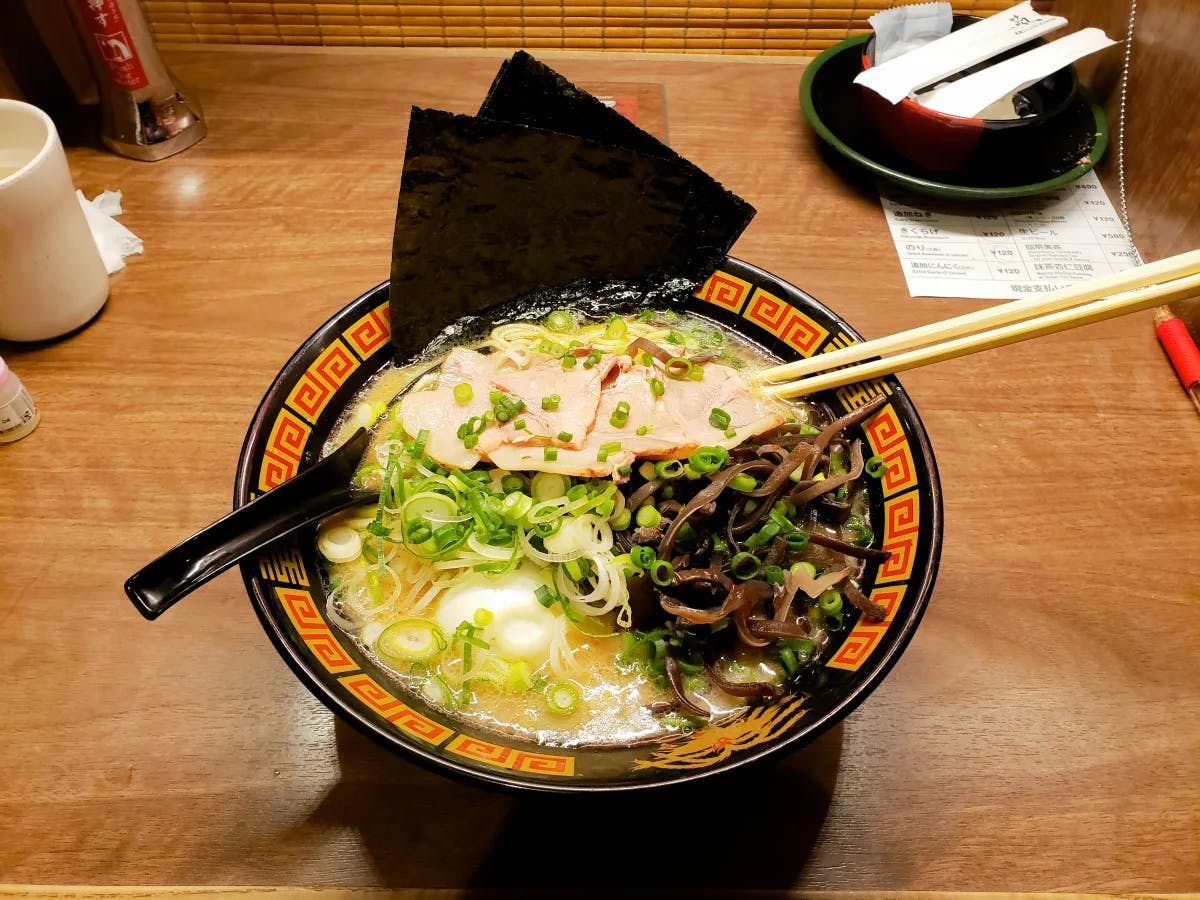 Ramen in a black ceramic bowl on a wooden table.