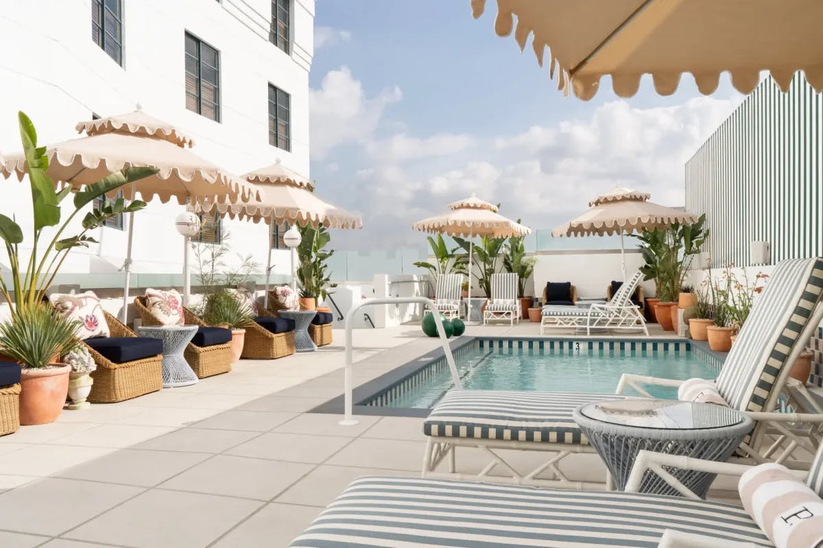 a sunlit pool terrace with pink umbrellas and plush striped loungers