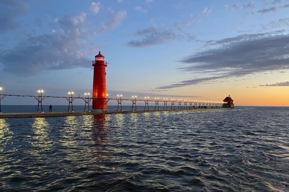 View of the red lighthouse and ocean at Grand Haven Pier at sunset.