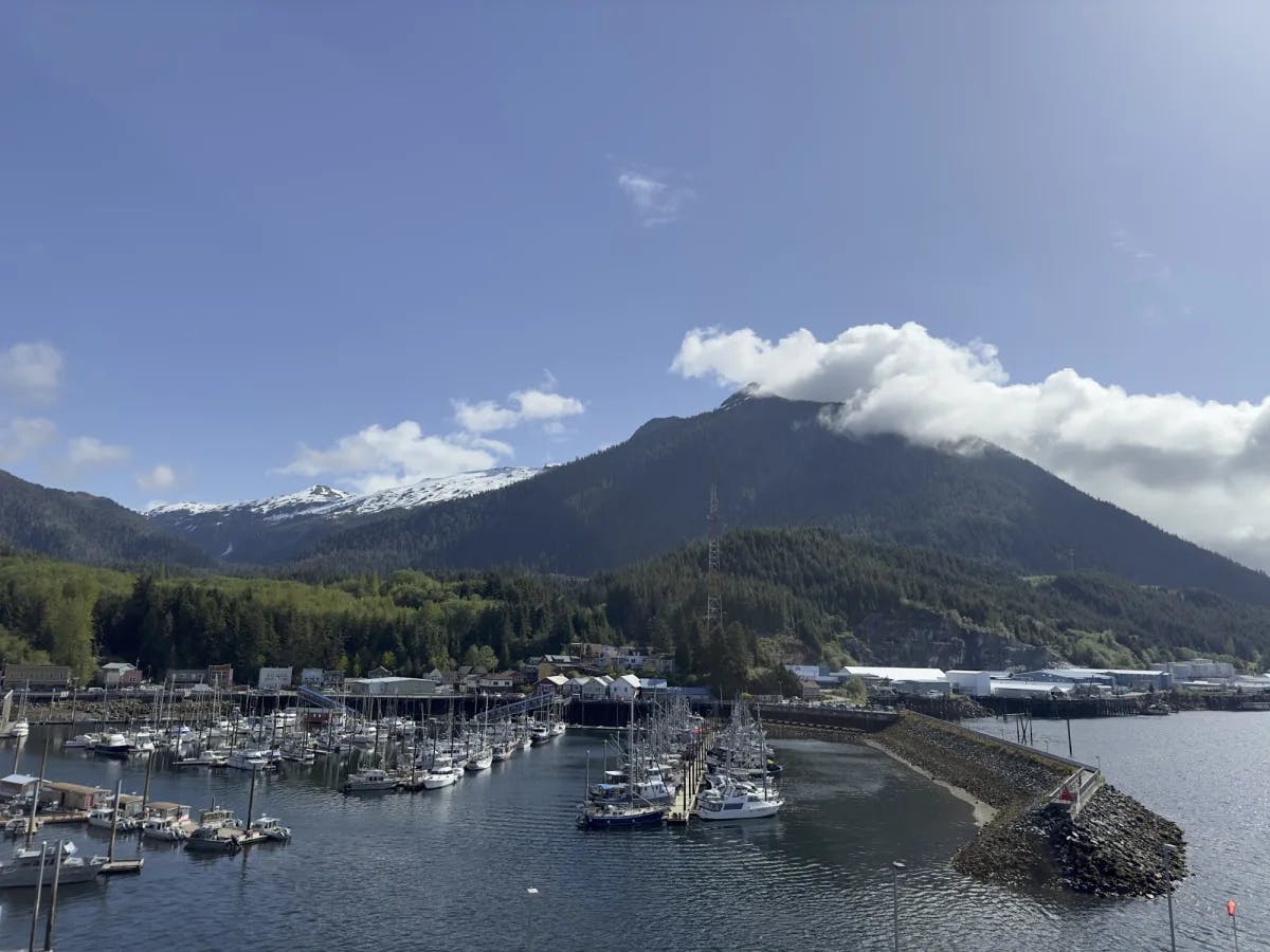 A harbor with boats parked in it and a large mountain in the background on a slightly cloudy day.