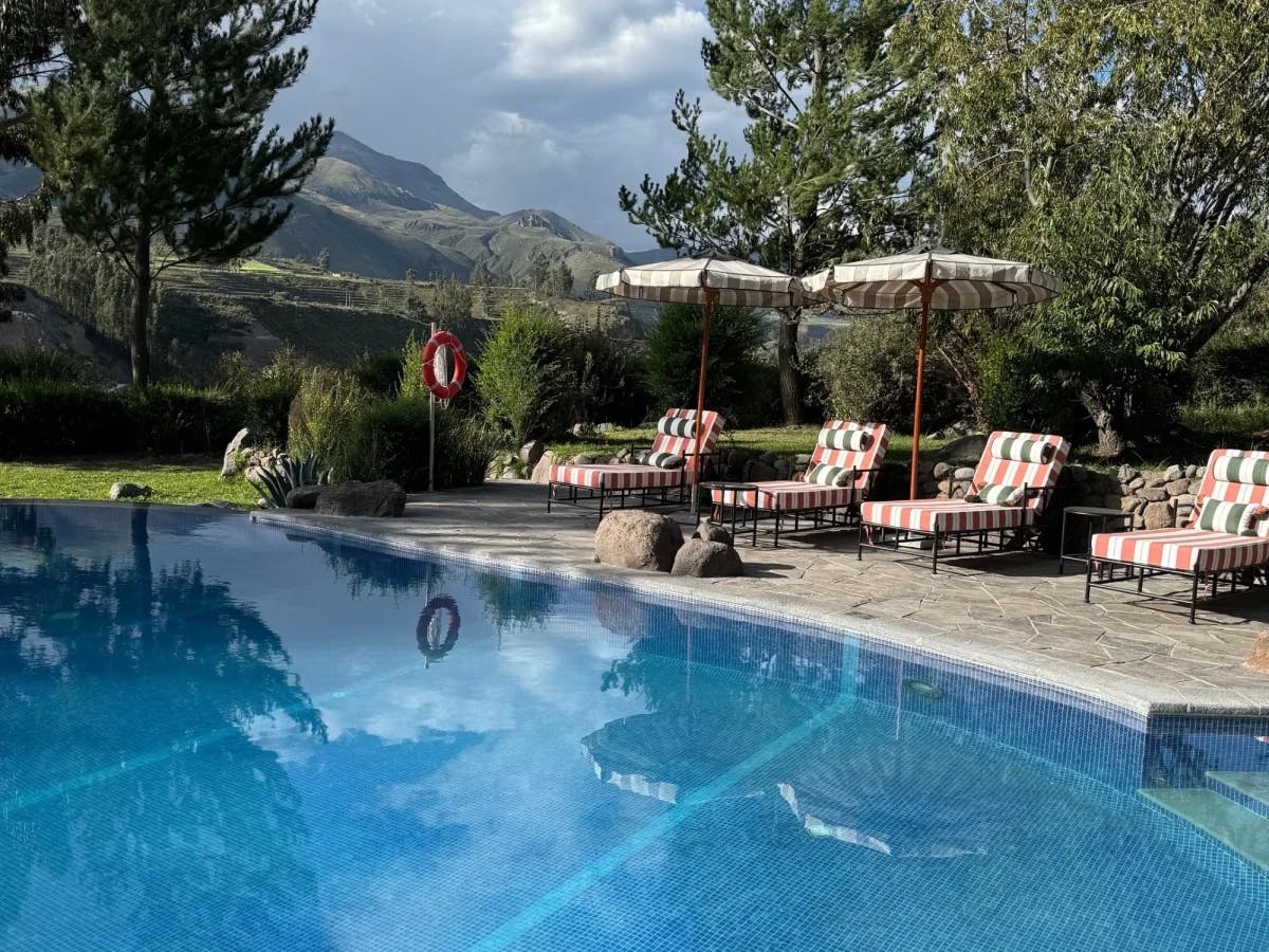 A view of the hotel pool, with cushy sun beds and umbrellas, surrounded by natural greenery and mountains in the distance.