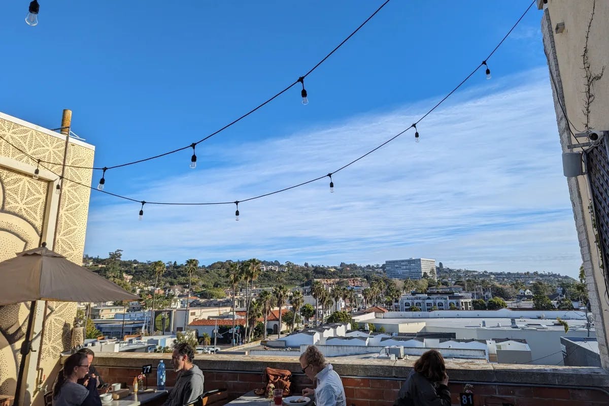 People sitting on a rooftop patio with the city and trees in the distance.