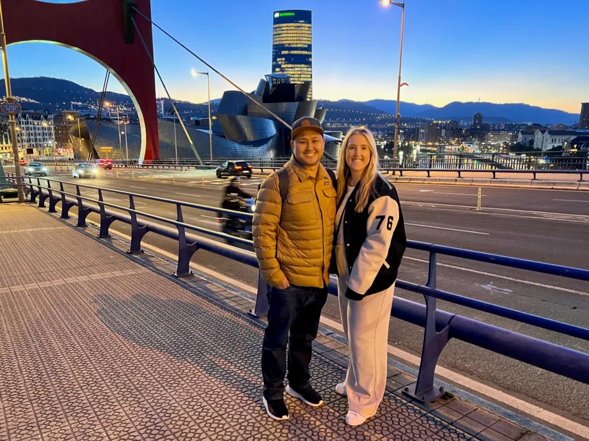 Man and woman posing for a photo on a bridge with city view in the background