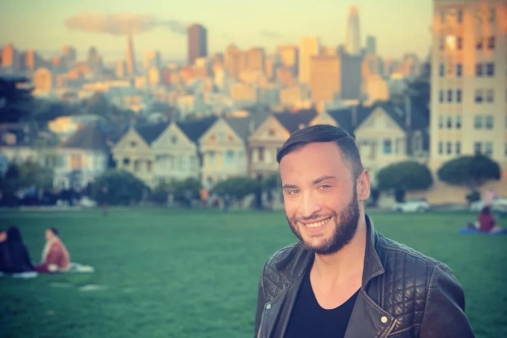 man with beard and leather jacket smiling with park and cityscape in the background