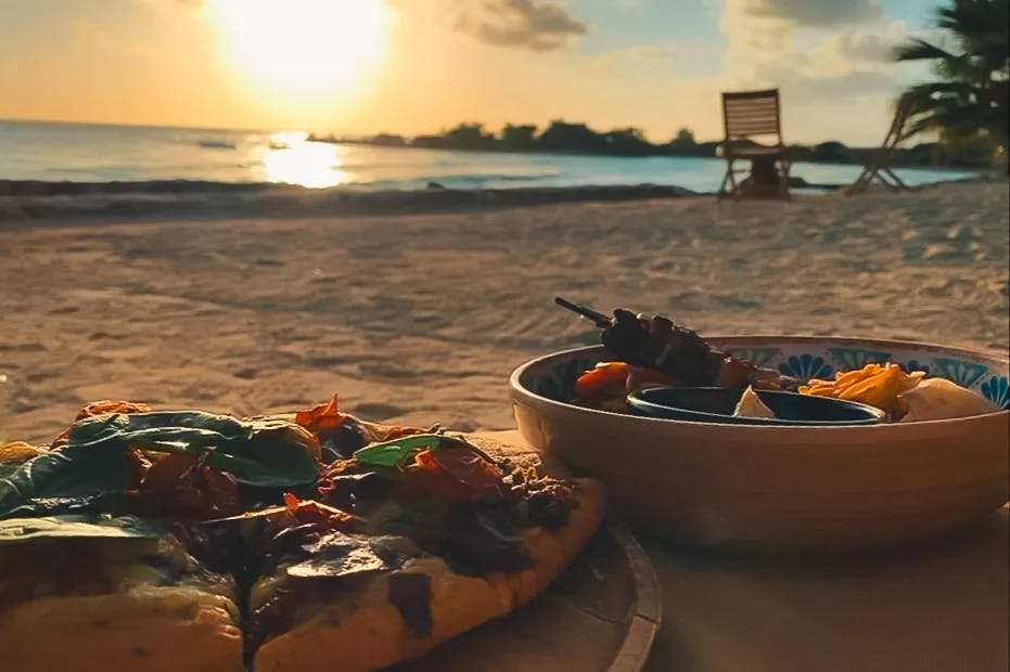 Plated food on a table in front of the beach, water and golden sunset.