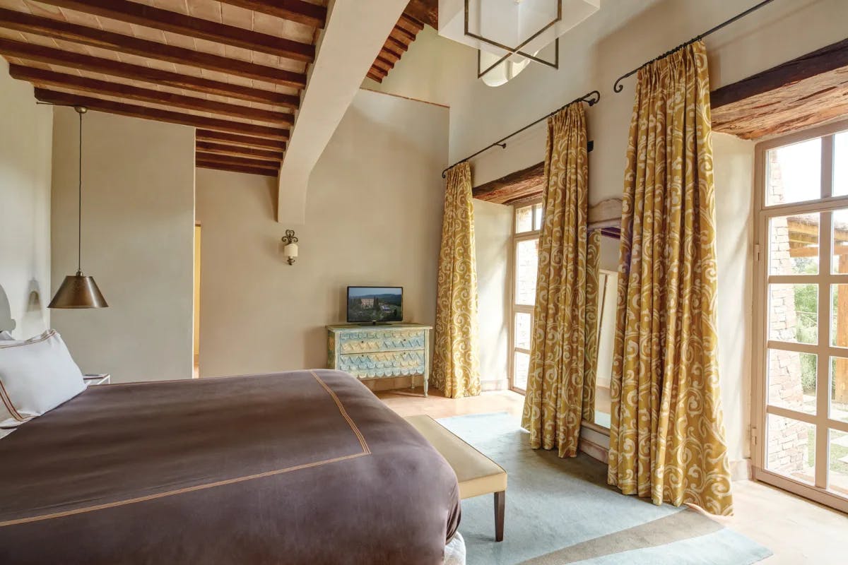 a bedroom with exposed ceiling beams and large windows flanked by heavy drapes