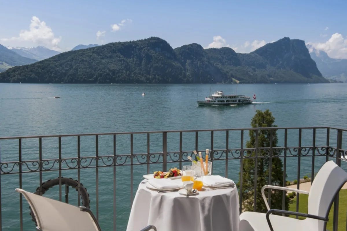 table for two on a terrace overlooking a lake with mountains and a large boat in the distance