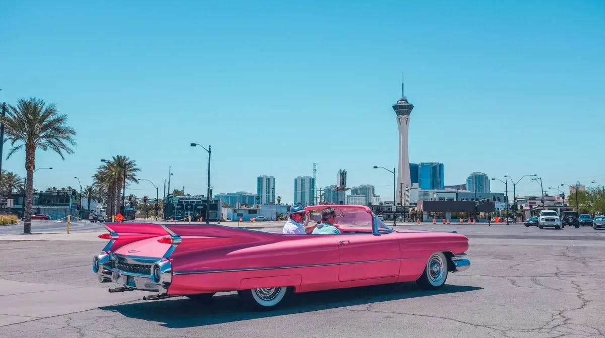 People riding in a pink car on a sunny day.