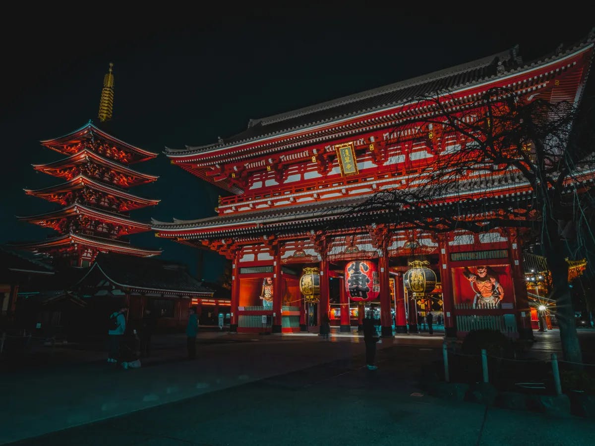 The image shows a brightly lit traditional Japanese temple and a five-storied pagoda at night, highlighting architectural details and cultural significance.