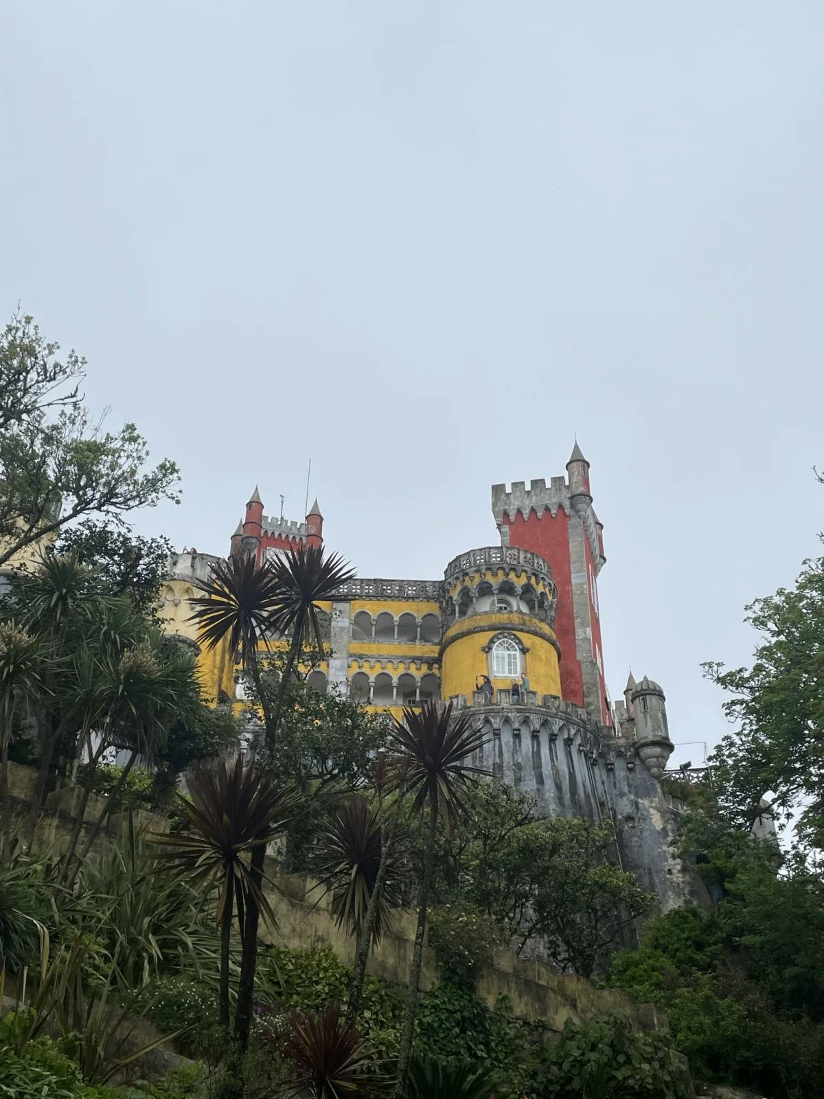 A view of the exterior of Palacio da Pena, surrounded by greenery and underneath a blue sky. 