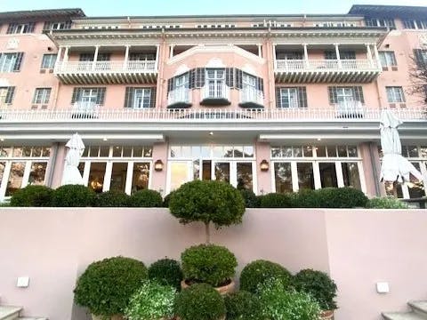 The image features a charming pink building adorned with multiple balconies, expansive windows and decorative greenery.