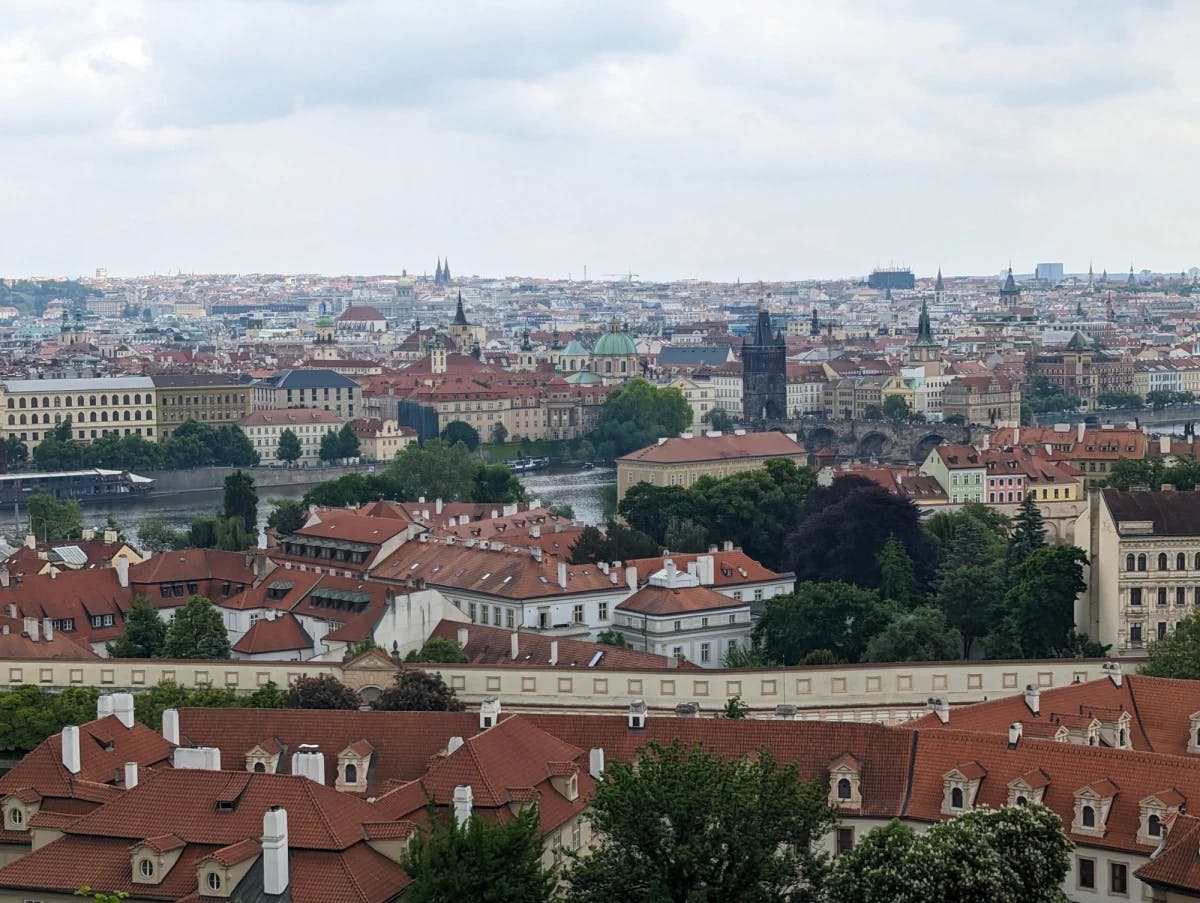 An overhead view of Prague at daytime complete with red roofed buildings and green trees. 