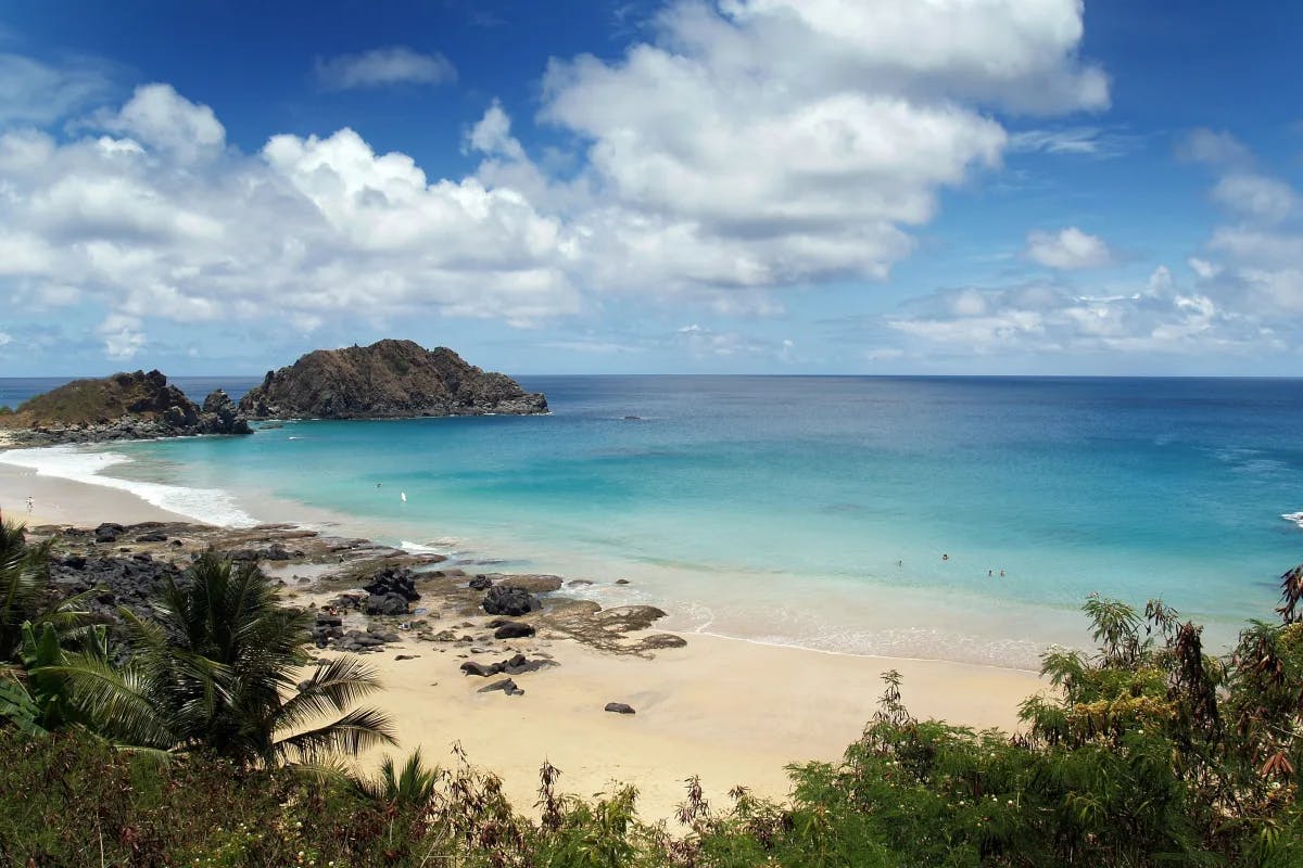 A view of the beautiful sandy beach surrounded by trees, turquoise blue waters and large rock formations. 