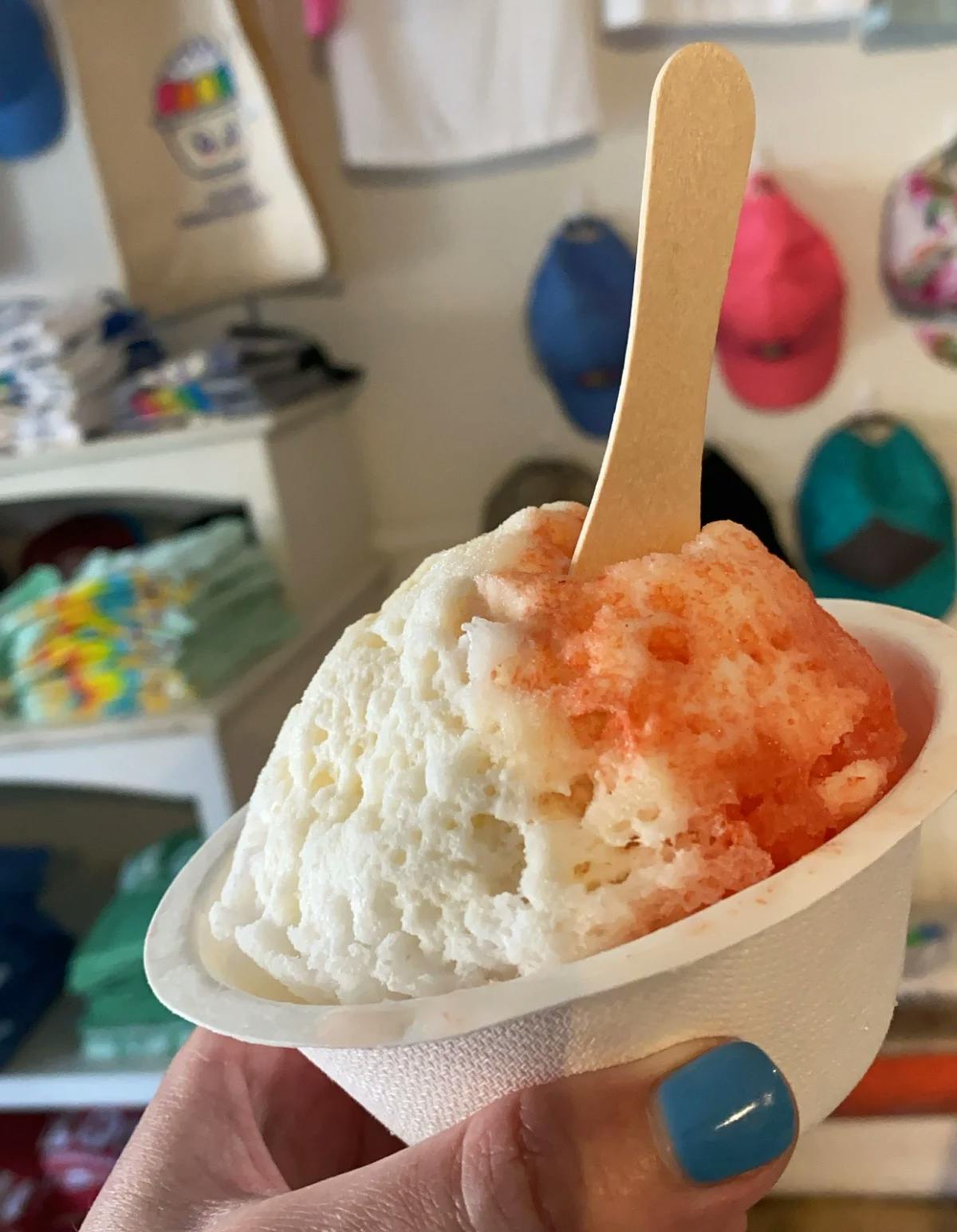 A bowl of shave ice held up for the camera in front of merch hanging on the wall.