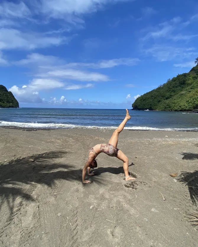 Annemarie doing a yoga pose on the beach outside at Honomanū Bay with water and volcanoes in the background.