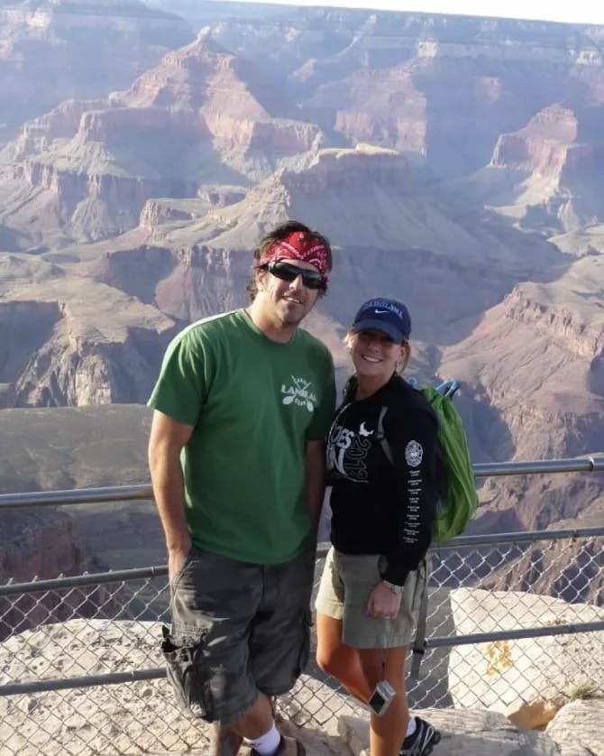 Shannon and a man posing in front of a fence with the Grand Canyon in the background. 