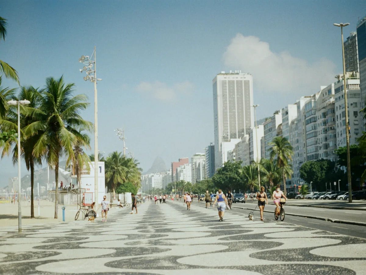 A lively beachfront promenade, bustling with people and lined with palm trees, under a clear blue sky.